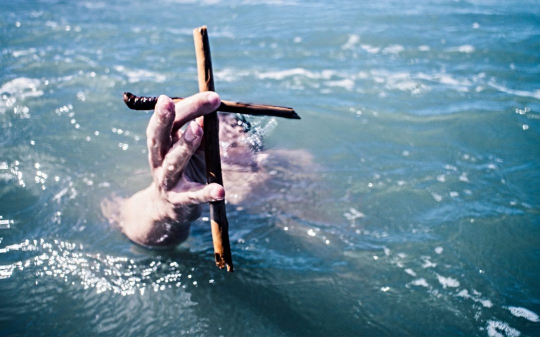 A man holding up a wooden cross in the water