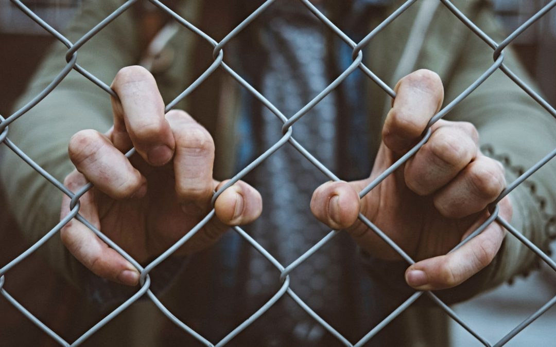 A man's hands gripping a chain-link fence