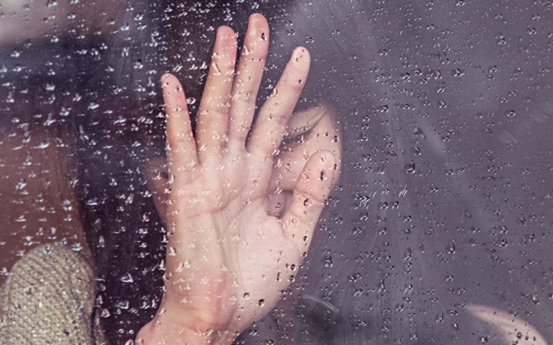 A women resting her hand on a window covered in water drops