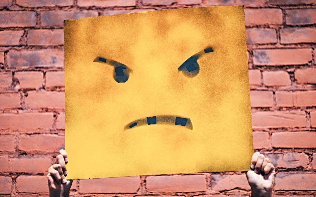 A sign with a frowning face in front of a red brick wall