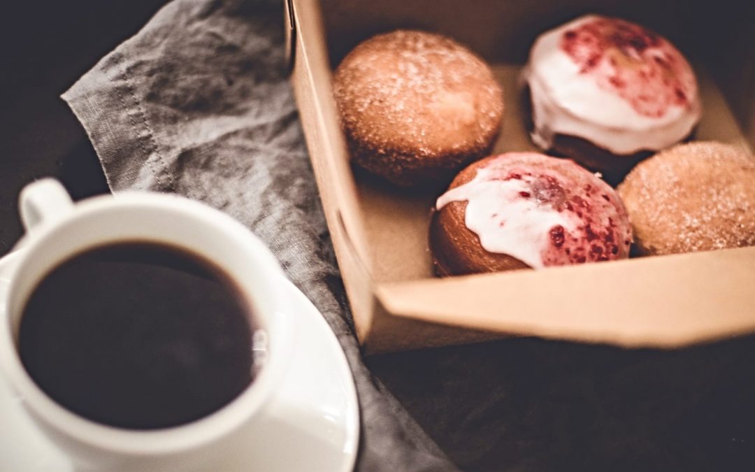 A cup of coffee in a white mug next to a box of donuts