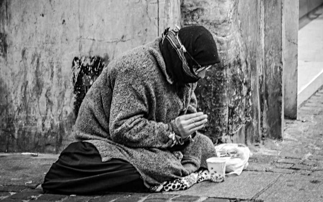 Homeless person sitting on sidewalk and begging
