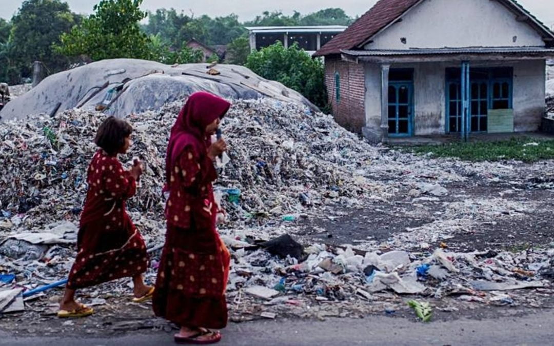 Two women walking by large pile of plastic waste