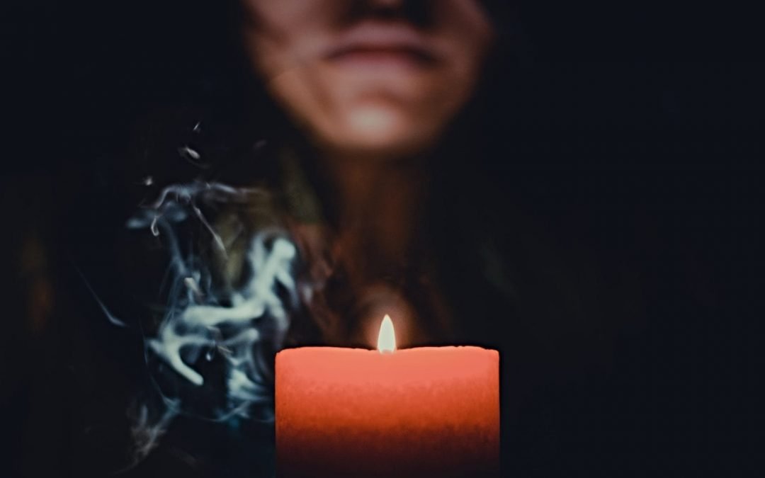Lit candle with lower half of face in background