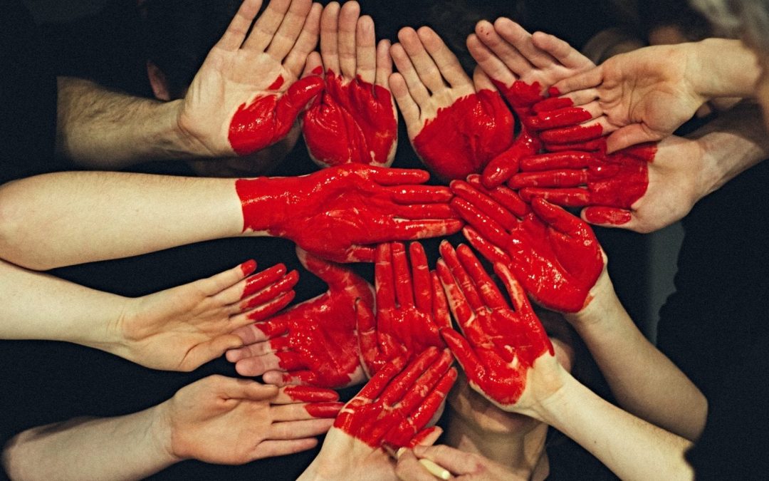 Hands clustered together with red heart painted on them