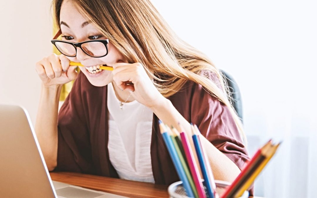 Woman biting pencil and looking at laptop