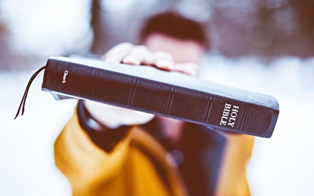 Man holding Bible outstretched toward the camera