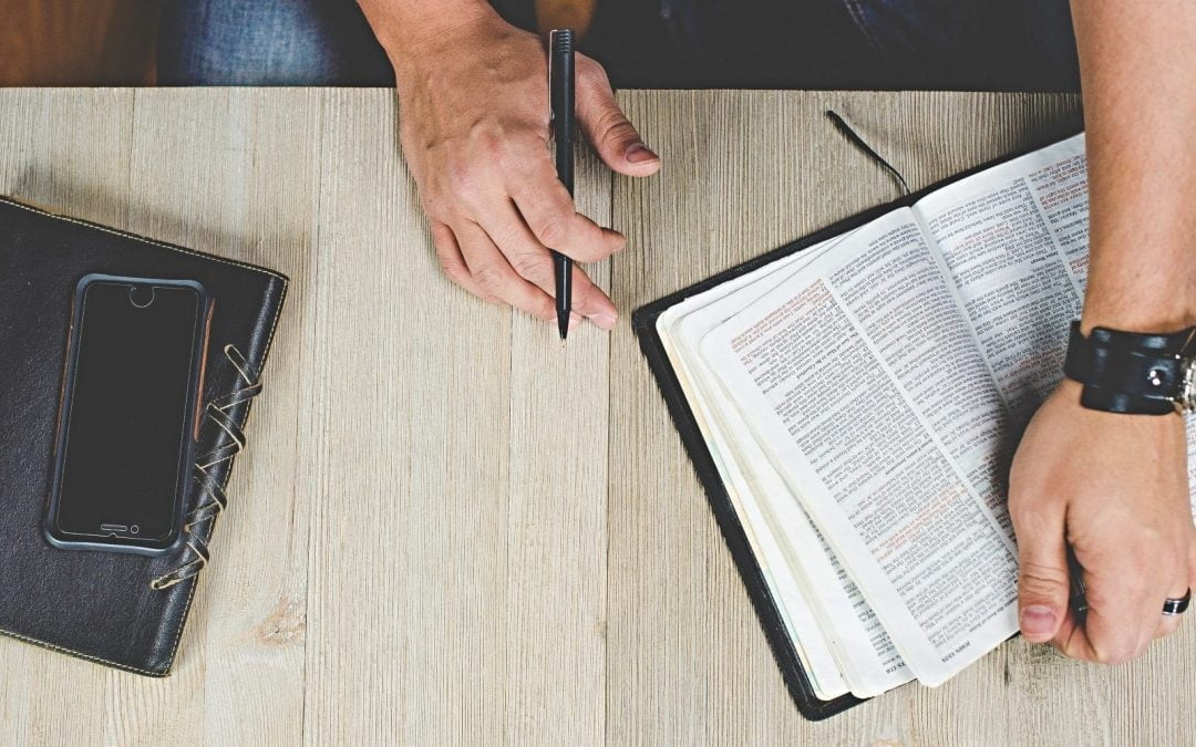 Man holding pen and open Bible on table