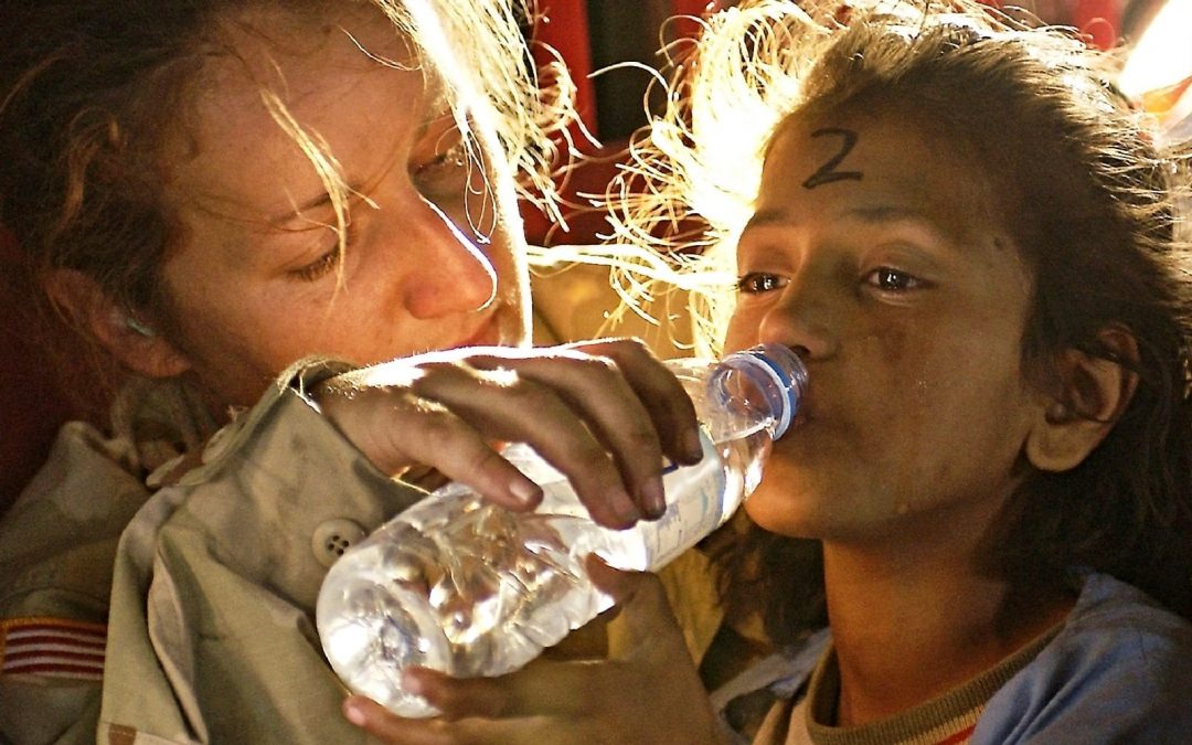 Woman providing drink of bottled water to girl