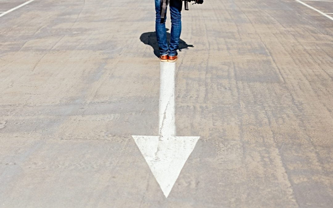 Person standing on downward white arrow painted on road