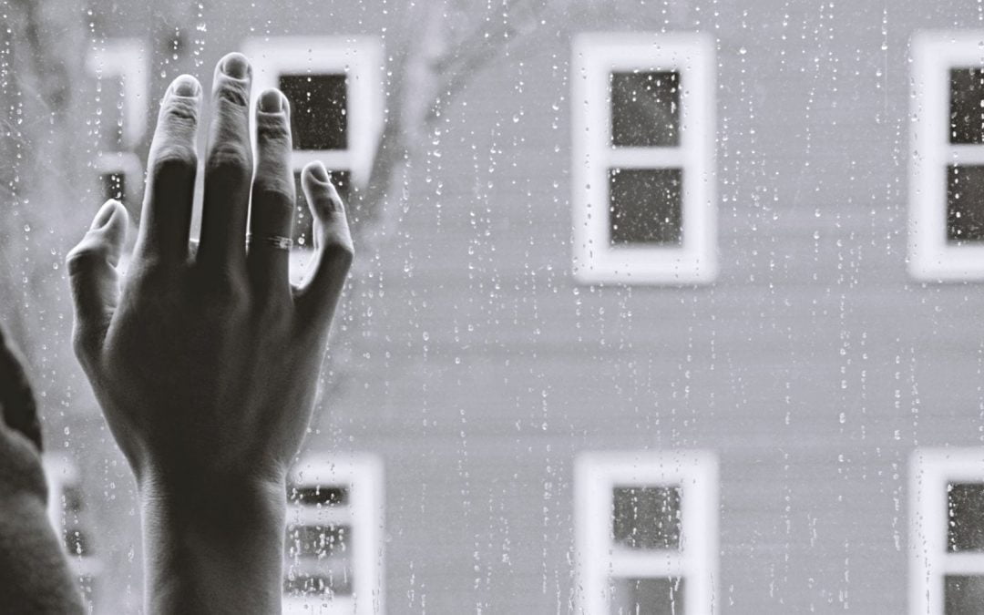 Hand on window splattered with raindrops