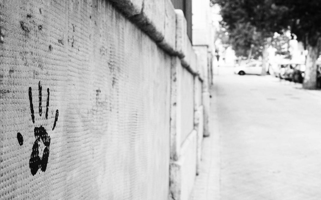 A handprint on a wall along an empty sidewalk.