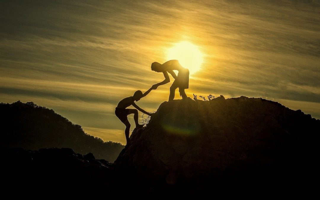 Silhouette of a man helping someone climb up a hill.