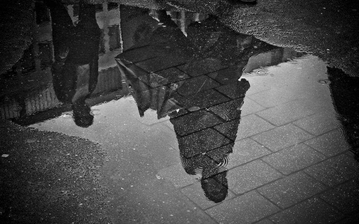 A reflection of two people in a puddle on a street