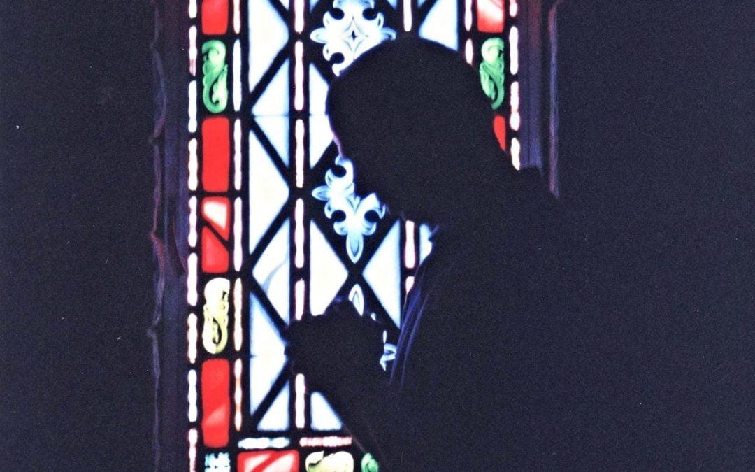 Silhouette of man praying in front of stained-glass window