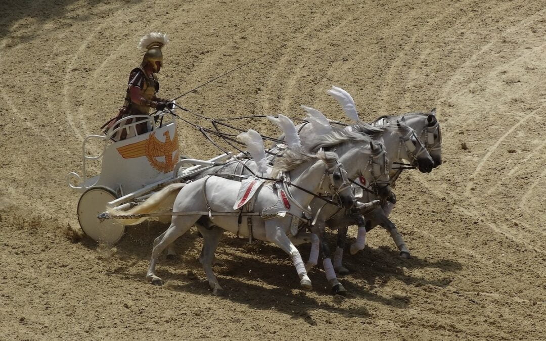 A man in a Roman style chariot pulled by four white horses.