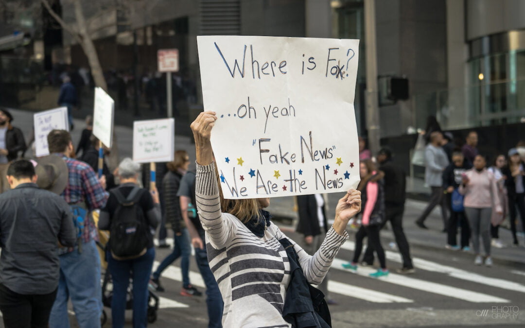 A woman on the street holding a sign about fake news.