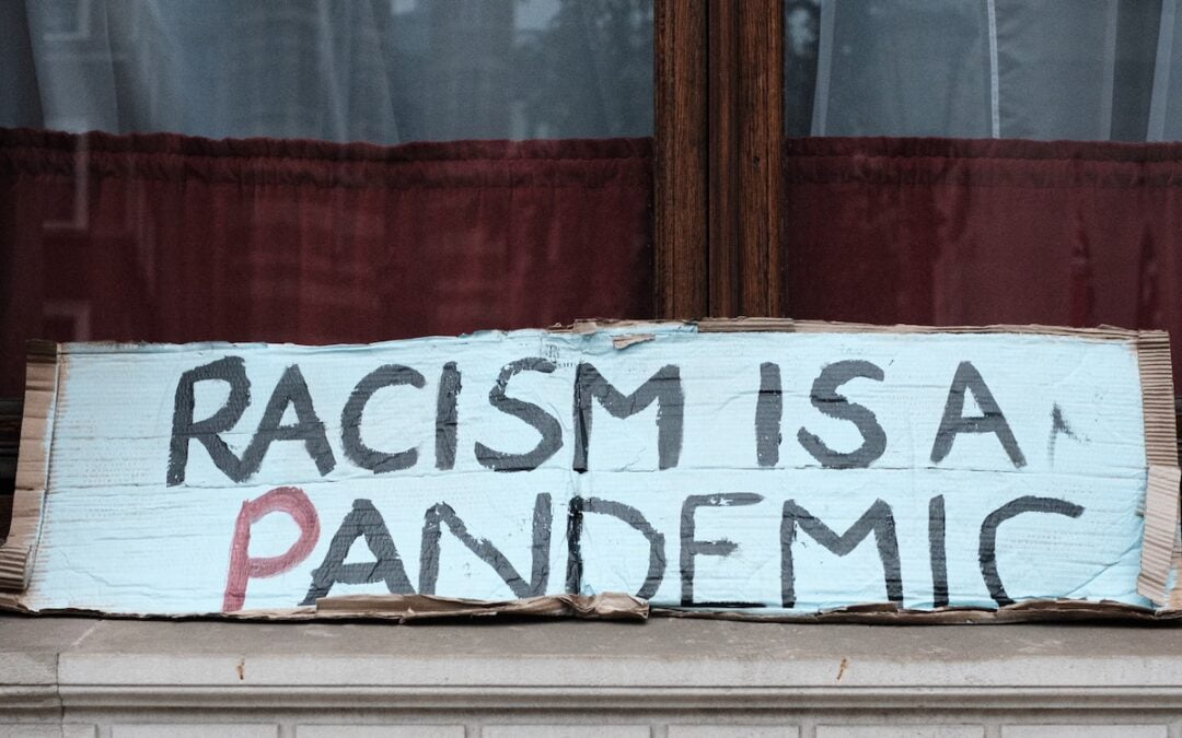 A cardboard signing sitting on a sidewalk that says, “Racism is a pandemic.”