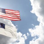 A flag pole with a U.S. flag flying above a Christian flag.