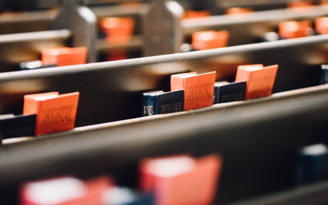 Rows of church pews with black Bibles and red hymnals.