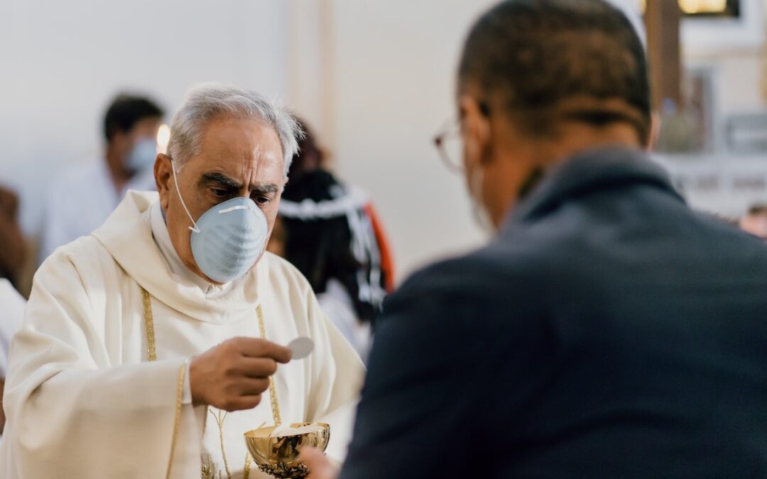 A priest wearing a mask offering communion to a worshipper during a church service.