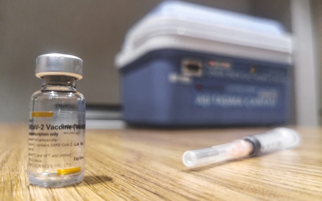An empty vaccine vial sitting on a table with a syringe next to it.