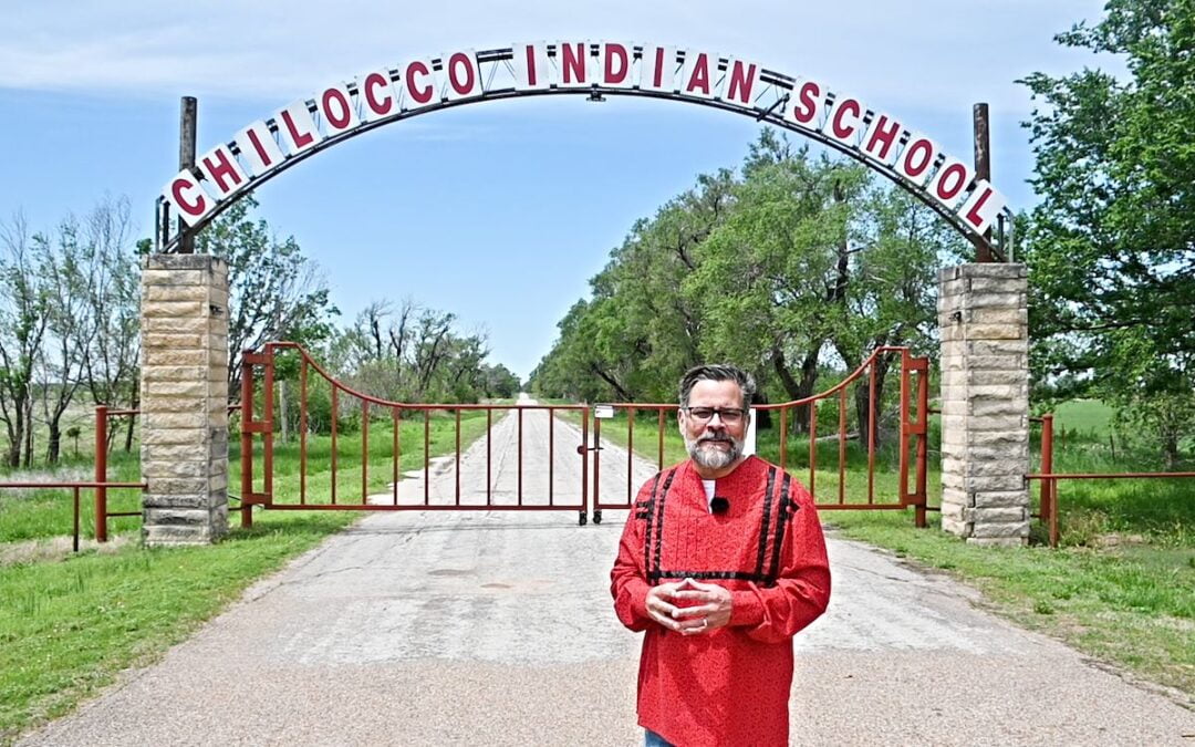 A man standing in front of the gates to Chilocco Indian Agricultural School.