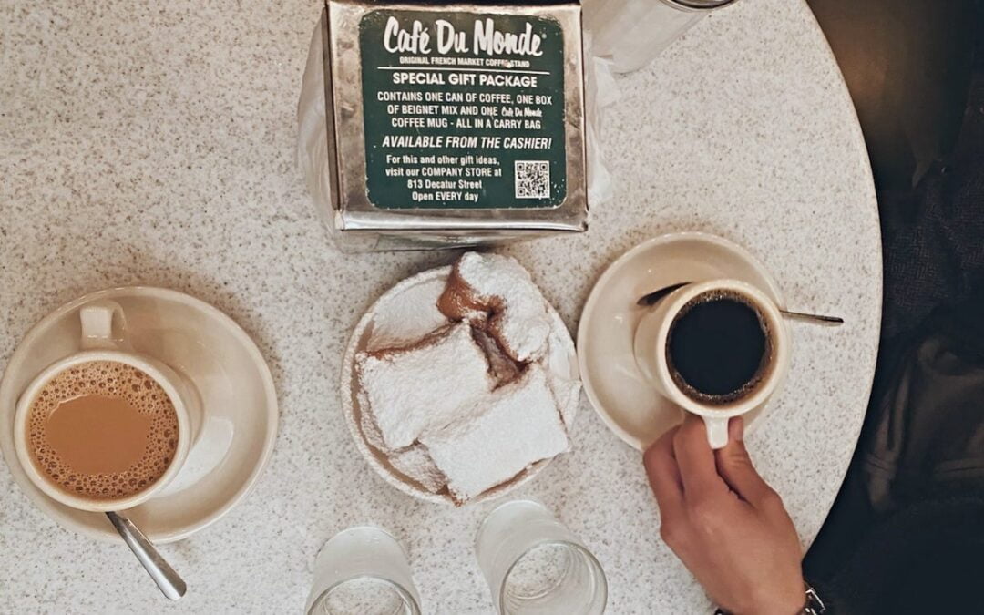 A bird’s-eye view of a table at Café du Monde with two glasses of water, a plate of beignets and two cups of coffee.