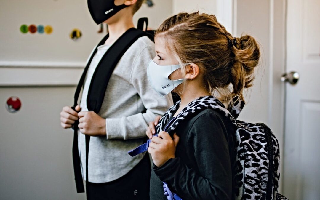 Two school-age children wearing backpacks and facemasks.