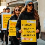 An anti-trafficking billboard seen from the street. // A group of people holding yellow signs at a demonstration calling attention to human trafficking.
