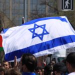 An Israeli flag in the center of the image with a Palestinian flag in the background to the left.