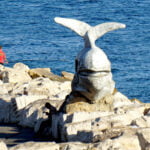 A whale statute amid rocks with water in the background.