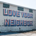 A cinder block wall with “Love Your Neighbor” spray painted on it.