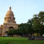 The front of the Texas Capitol building with trees lining the sidewalk.