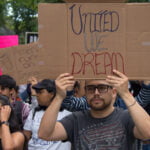 People at a march to support the DACA program with one man holding a sign that says, “United we dream.”