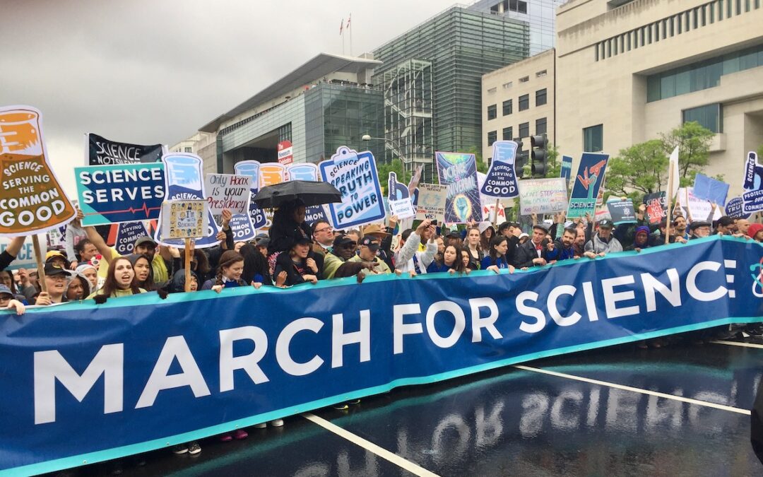 People on a street holding signs and a banner advocating for science funding.