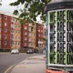 A street scene with a sign on a post that has “We Are One” on it multiple times.