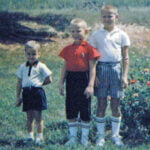 Three boys standing outside next to a rosebush.