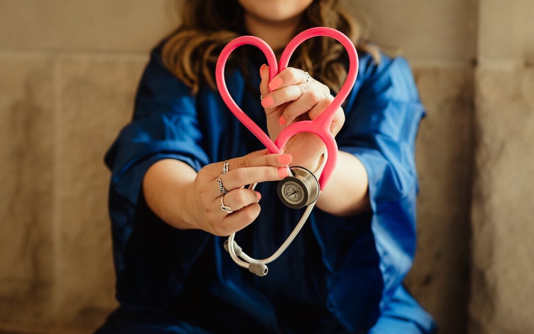 A woman with a stethoscope and forming the tube into the shape of a heart.