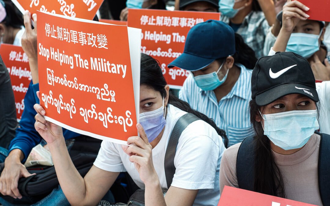 People wearing masks and holding signs protesting the military coup in Myanmar.