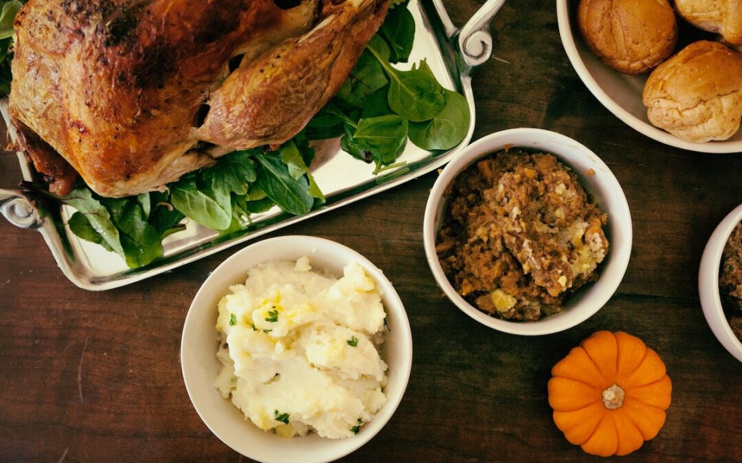 A turkey seen from above sitting on a wood table next to a side of dressing, mashed potatoes and rolls.