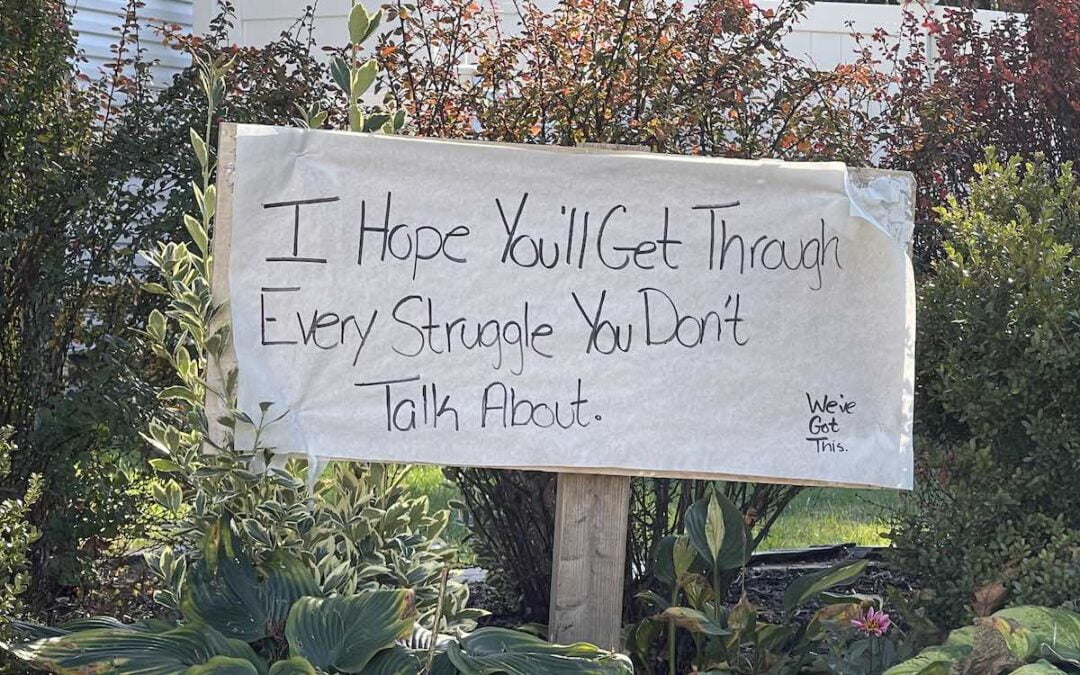 A sign in a flower bed offering a word of encouragement to passersby.