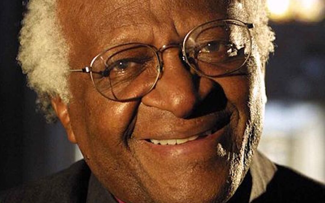 A closeup photo of Desmond Tutu smiling and wearing glasses.