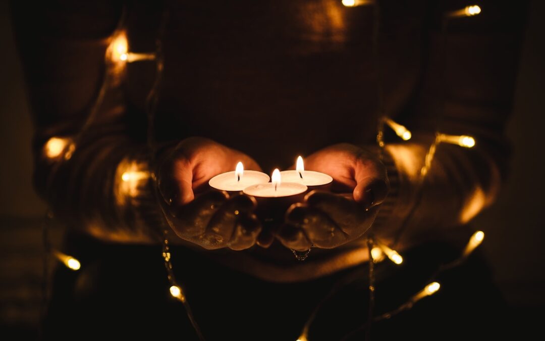 A person standing in the dark holding three small lit candles.