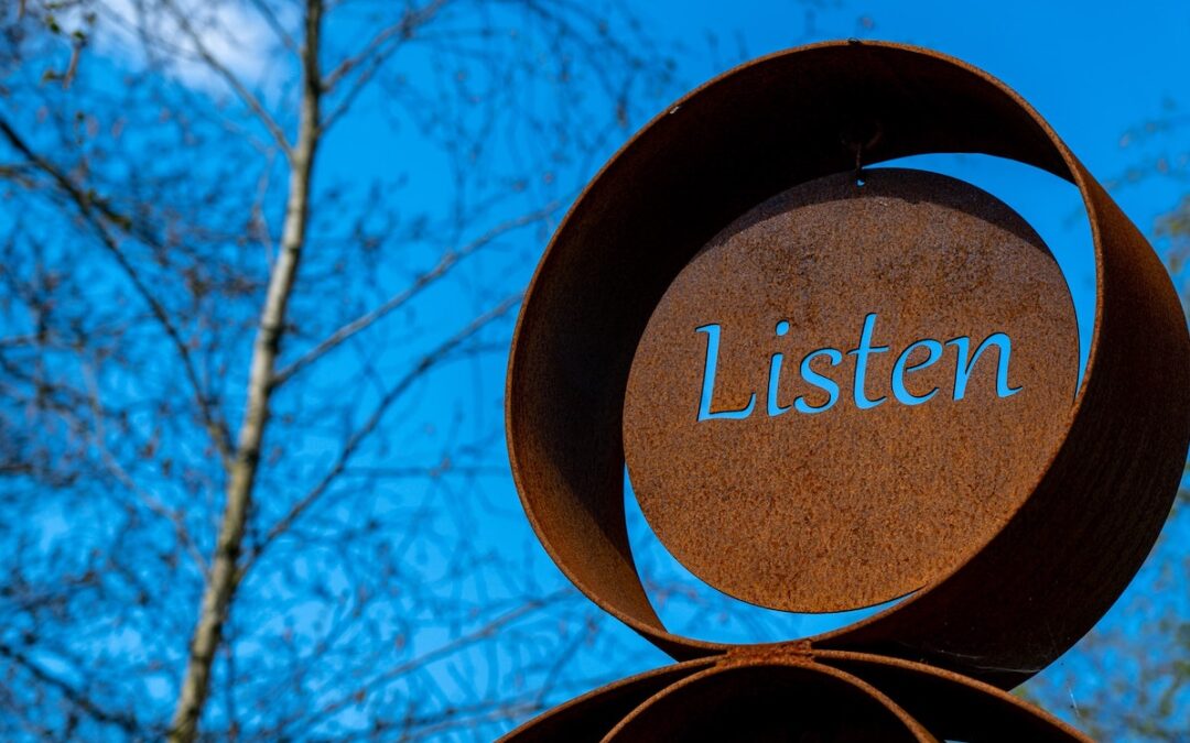 A brown metal sign with the word “Listen” engraved into it.