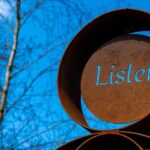A brown metal sign with the word “Listen” engraved into it.