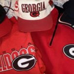 Three hats and two shirts with the University of Georgia logo on them.