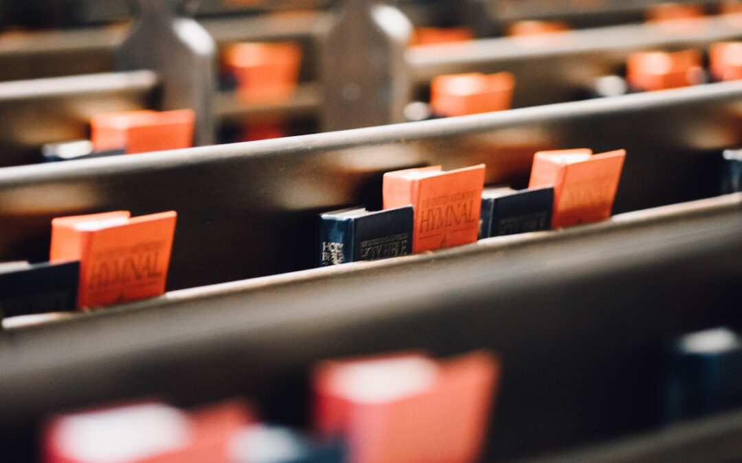 A row of pews in a church with red hymnals and black Bibles in a wooden slot on the back of each row.
