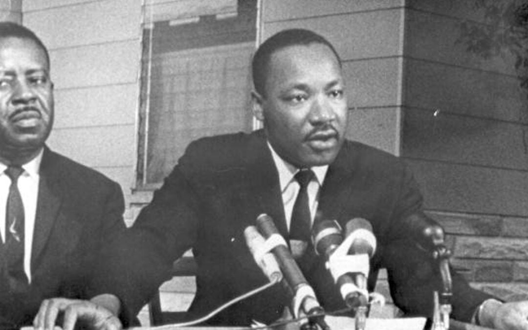 A still photo of Martin Luther King, Jr. speaking from a podium in St. Augustine, Florida, in 1964, with Ralph Abernathy standing off to the side.