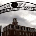 The exterior of a building in the background with a metal arch in the foreground over the sidewalk entrance with the words “Arkansas Baptist College.”